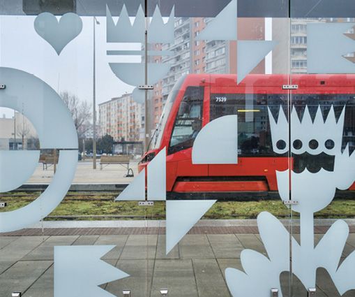 Sklenená mozaika prístreška na električkovej zastávke Jungmannova s motívmi maľby Znaky Bratislavy. V pozadí ide červená električka na linke číslo tri.